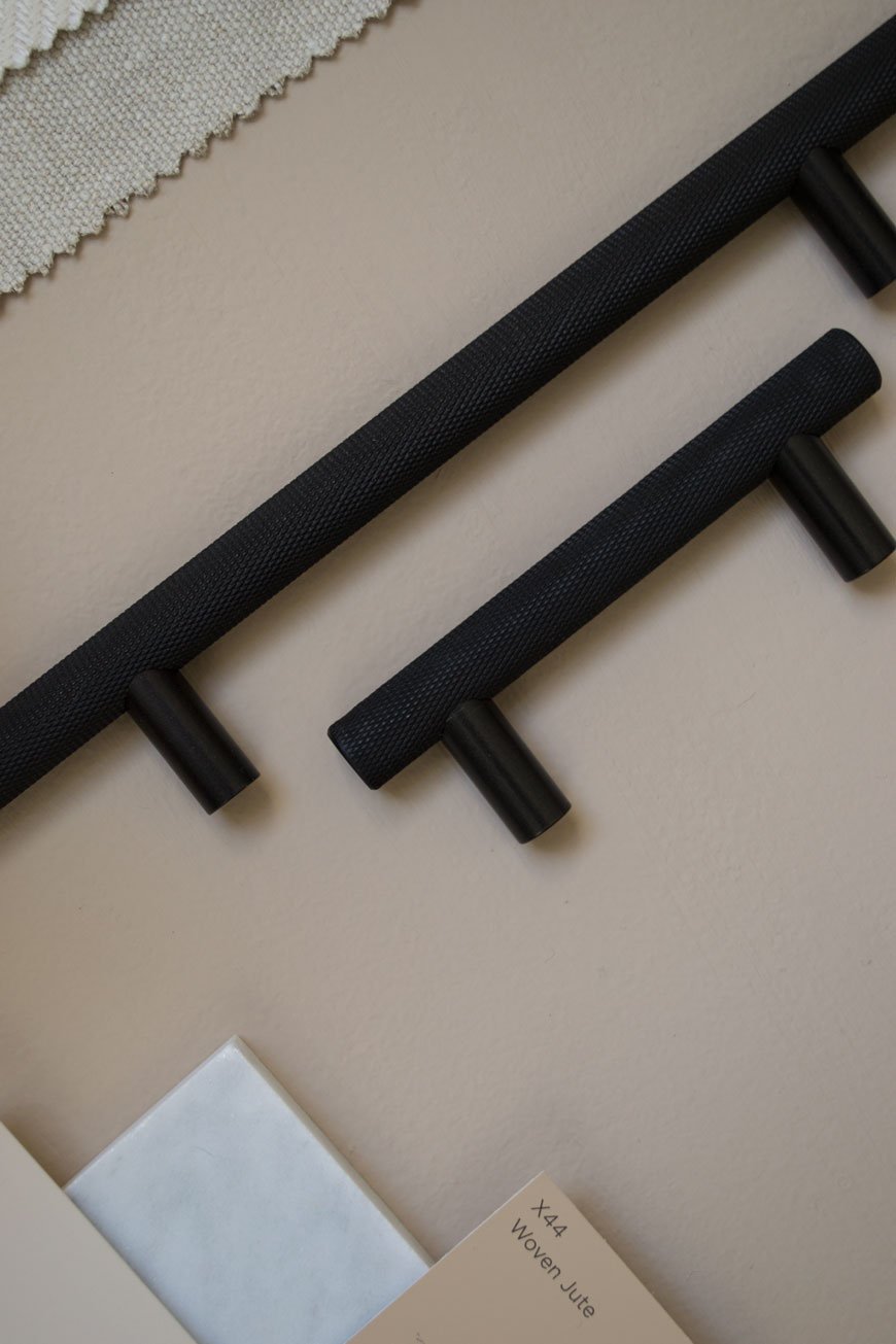 Black metal cupboard door handles with a textured surface on a moodboard for a beige bedroom scheme.