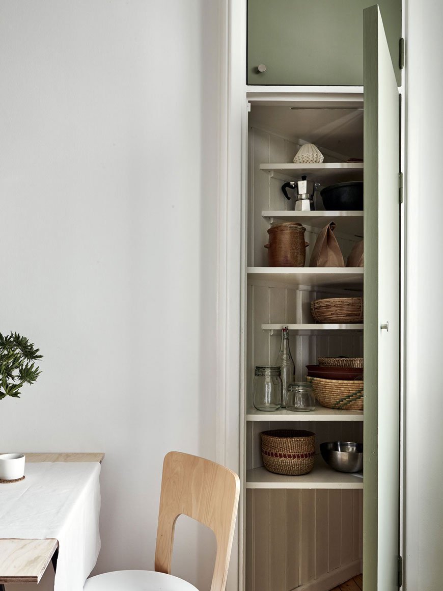 A corner storage cupboard in a kitchen with green kitchen units. 