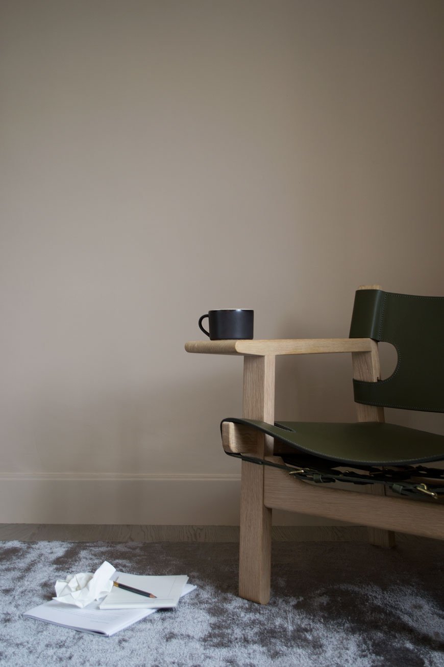 A black mug sits on the wide arms of The Spanish Chair, produced by Fredericia.