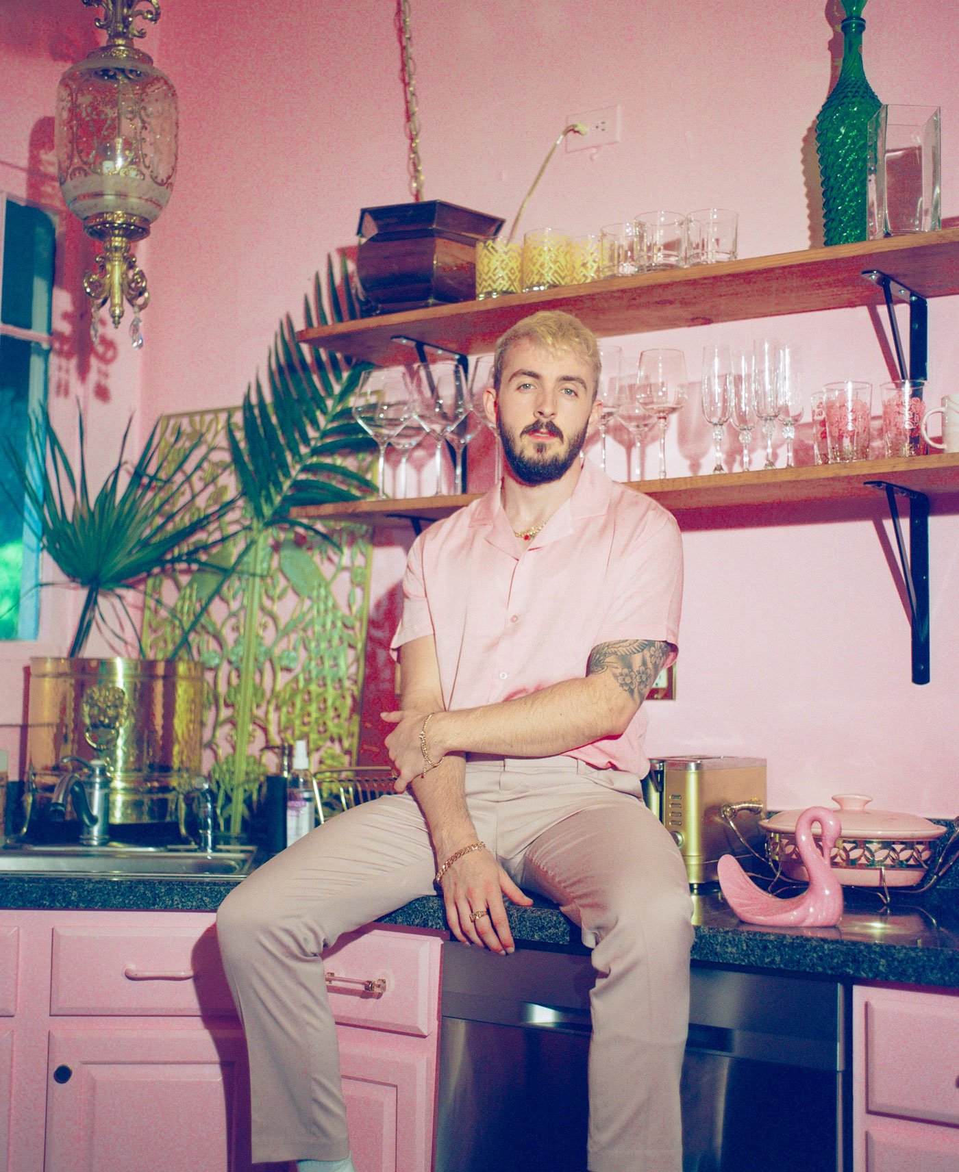 r&b singer alex slay sitting on kitchen counter wearing pink shirt