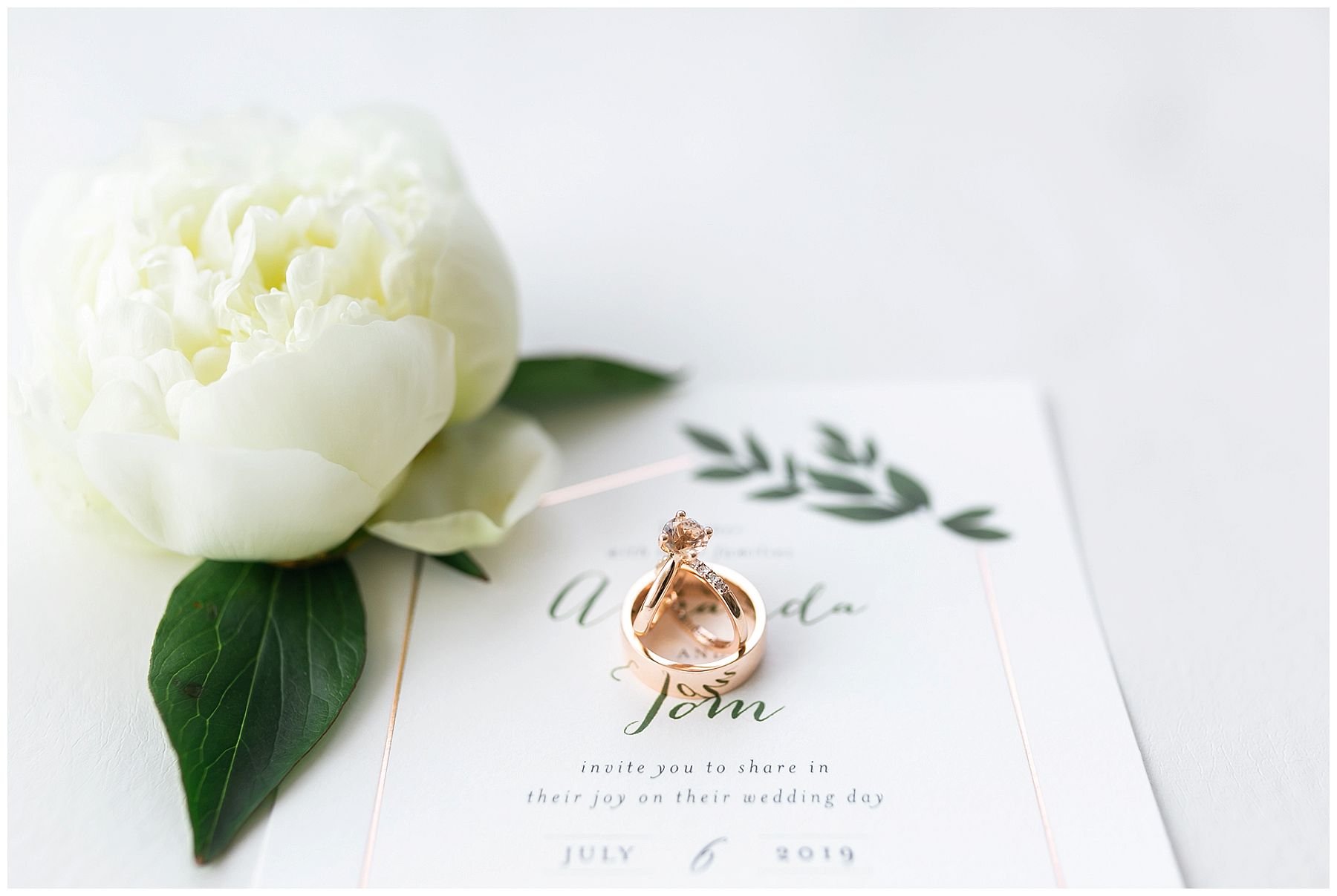 Bride's rose gold wedding rings on invitation suite with white peony