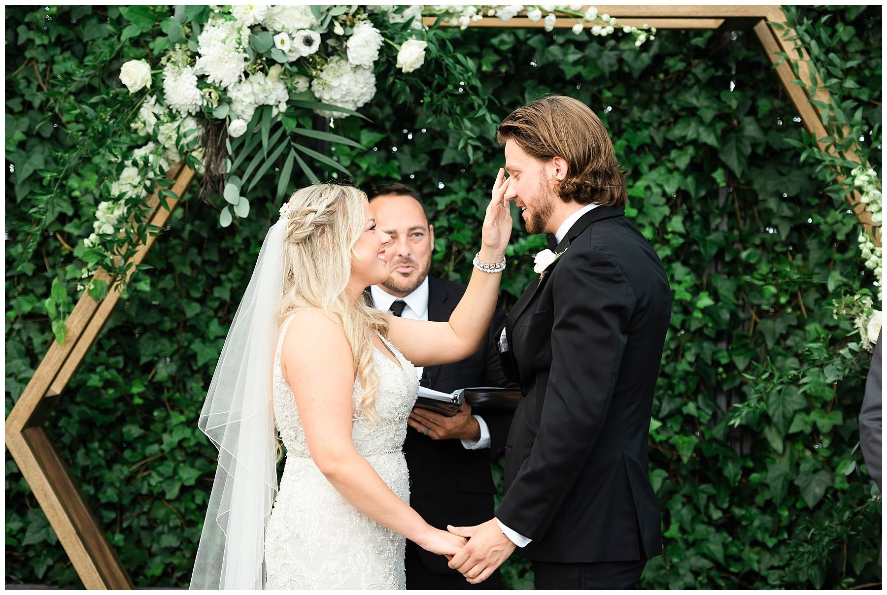Bride wiping the tears off groom's face during their greenhouse ceremony 