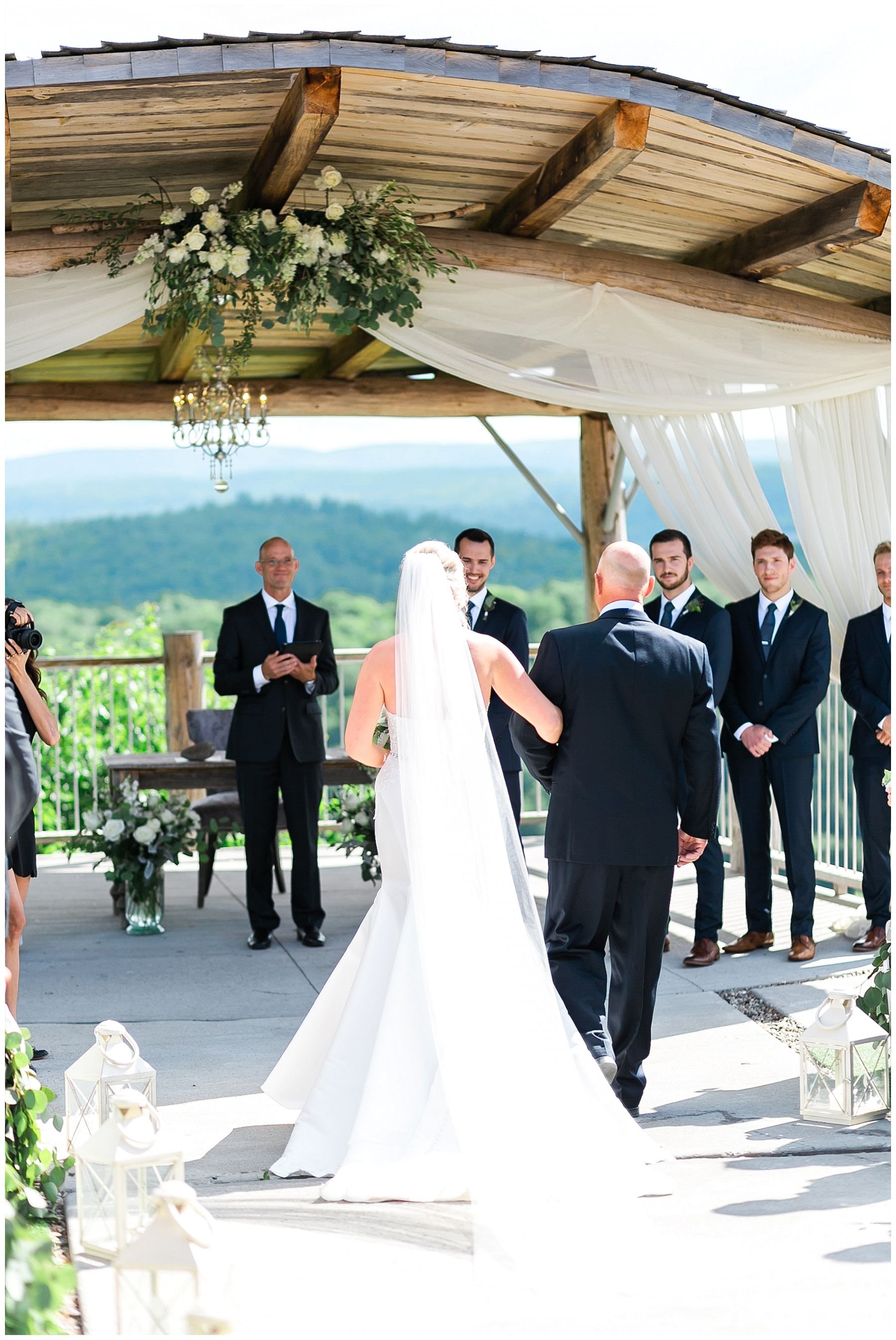 Bride walking down the aisle in outdoor ceremony under the arch cliffside