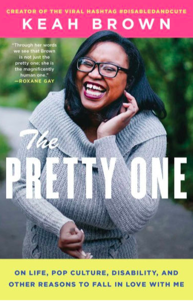 Cover of Keah Brown's The Pretty One, with author name in white on a pink field at the top, above a picture of Keah, wearing glasses and laughing as she curls some hair behind her ear. She is wearing a gray cowl-necked sweater, and her other hand is curled in front of her stomach. The background is a blurred forest scene beside a roadway.