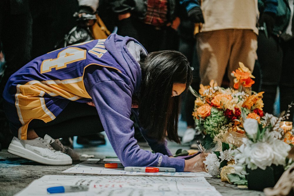 Young woman wearing a Kobe Bryant jersey writing a note on a memorial at Staples Center in Los Angeles.