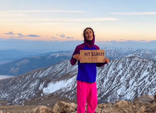 Flamingo up a mountain on the CDT holding a summit sign in a hoodie