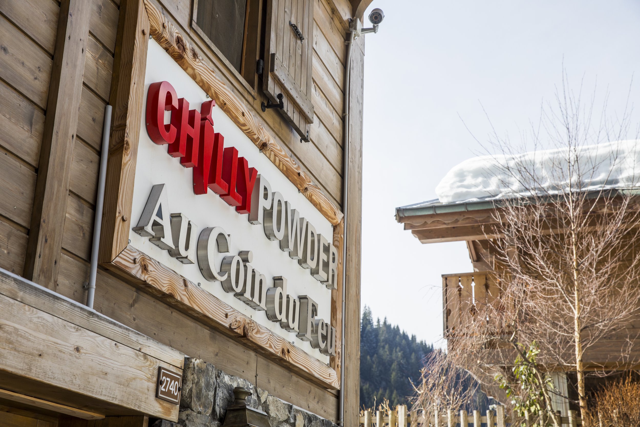 A sign on the wall of a wooden Alpine Hotel with the name 'Chilly Powder' in red and grey.