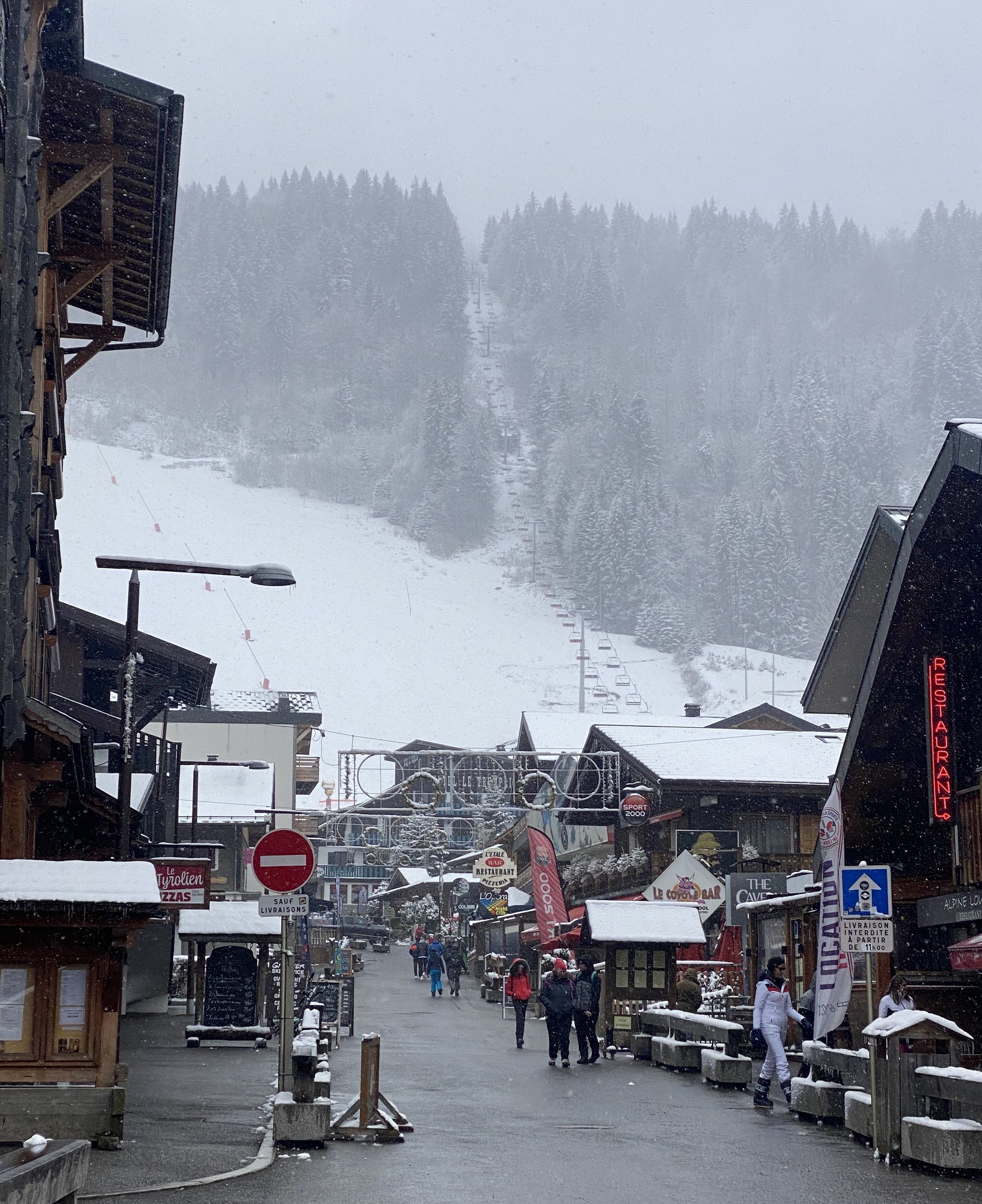 View of a Morzine street in the snow showing the slopes and ski life behind