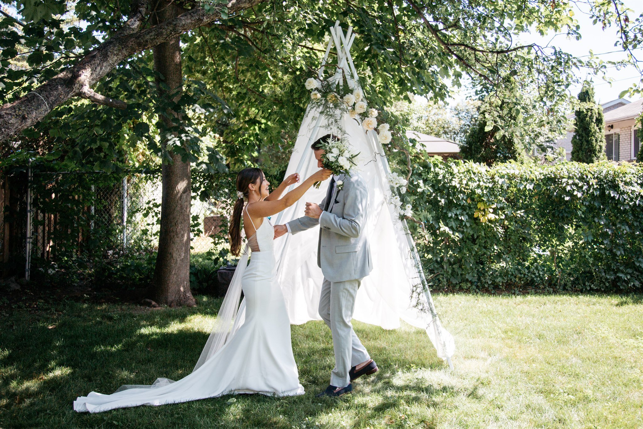 Intimate backyard wedding. Bride and groom photographed outside with flowers. 