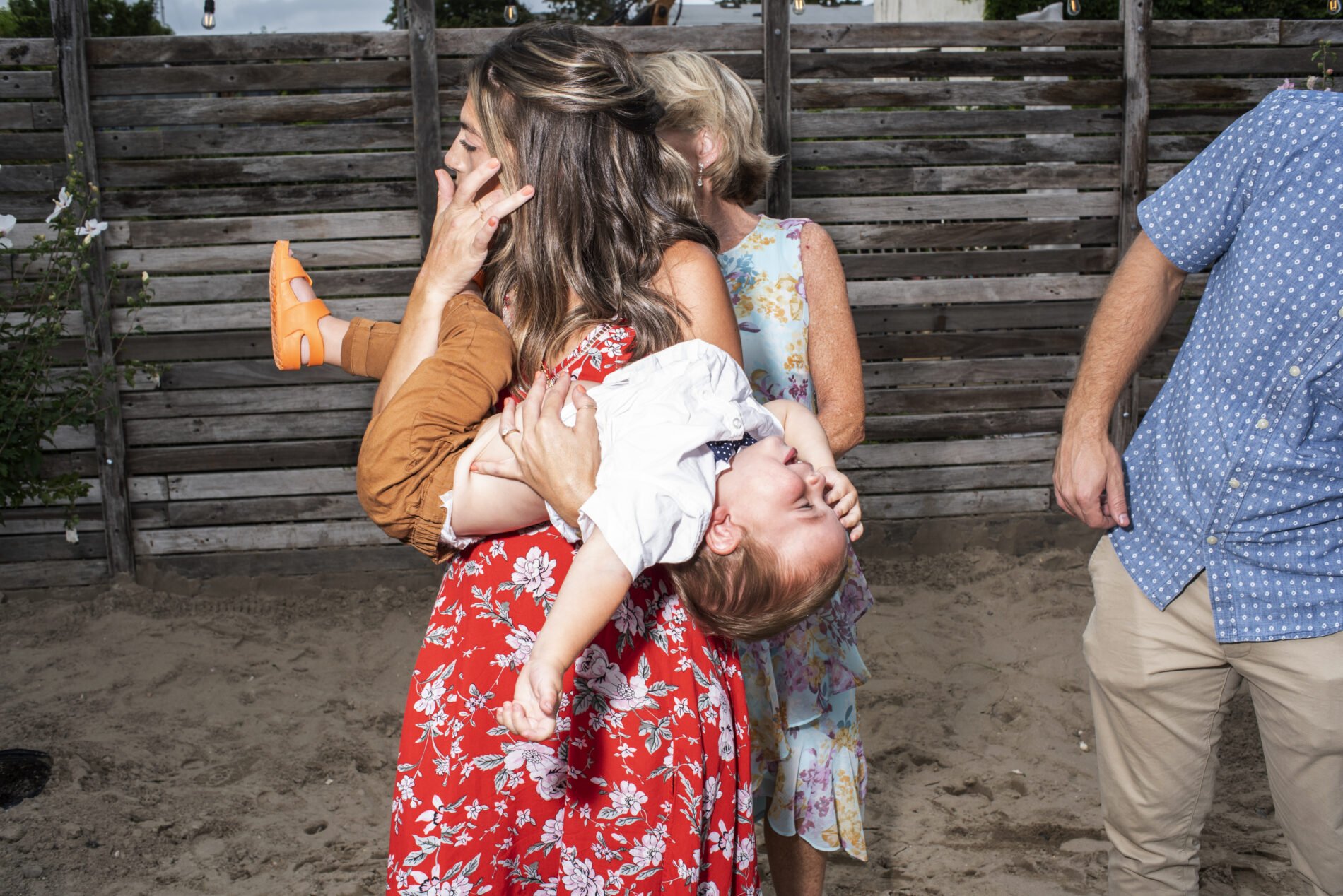 Beach Wedding Photography. Mom at a summer wedding holding her toddler in Far Rockaway, NY. Shot by Angela Cappetta NYC Wedding photographer with a Nikon DSLR.