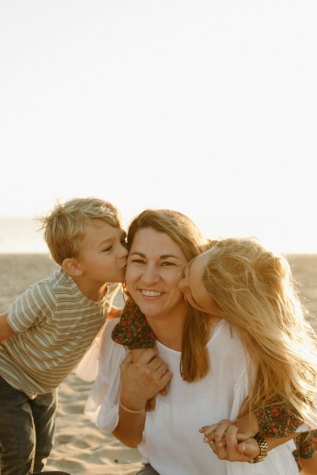 Kids kissing their mom on the cheek at the beach