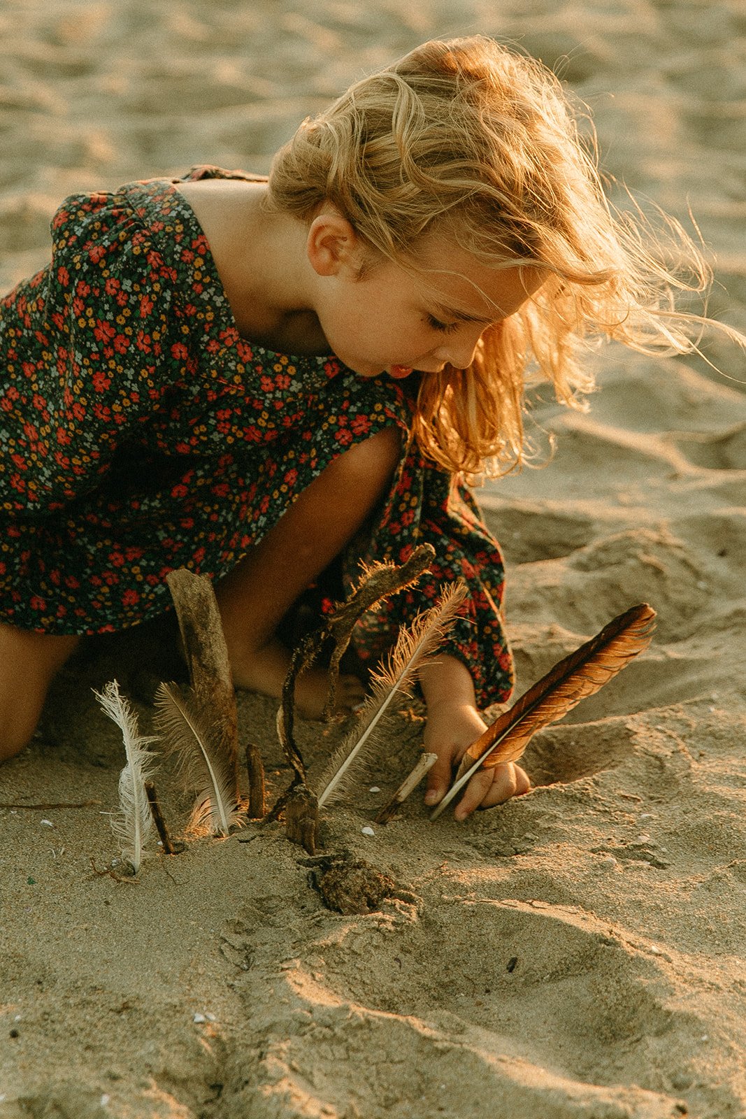 Little girl picking up feathers on the beach during a family photoshoot