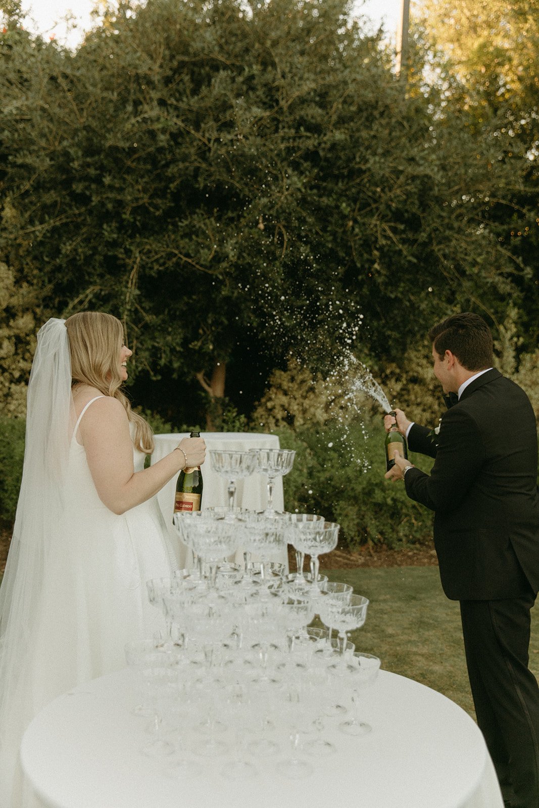 Bride and groom popping champagne near a champagne tower