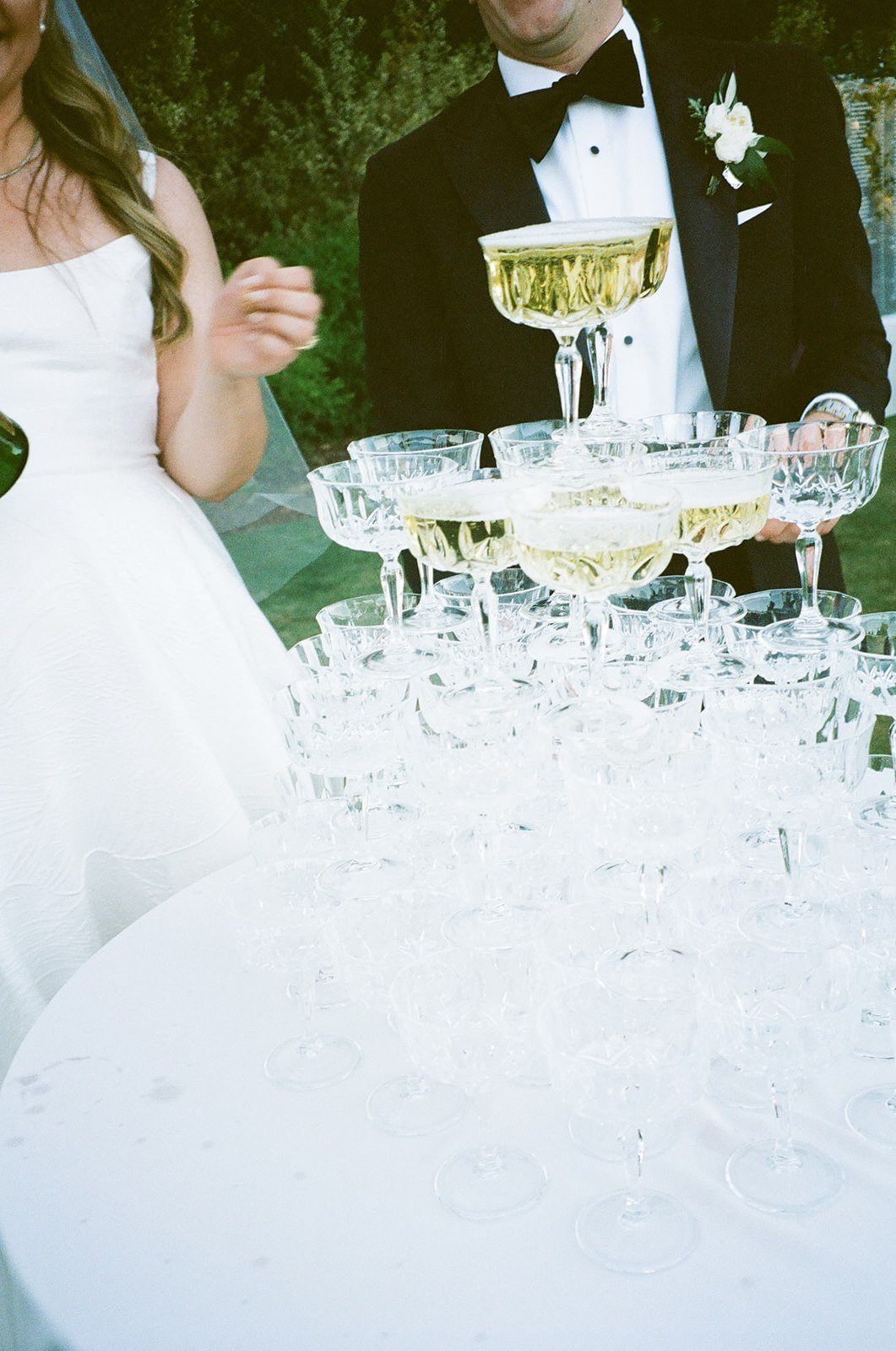 Film photos of bride and groom pouring champagne on champagne tower