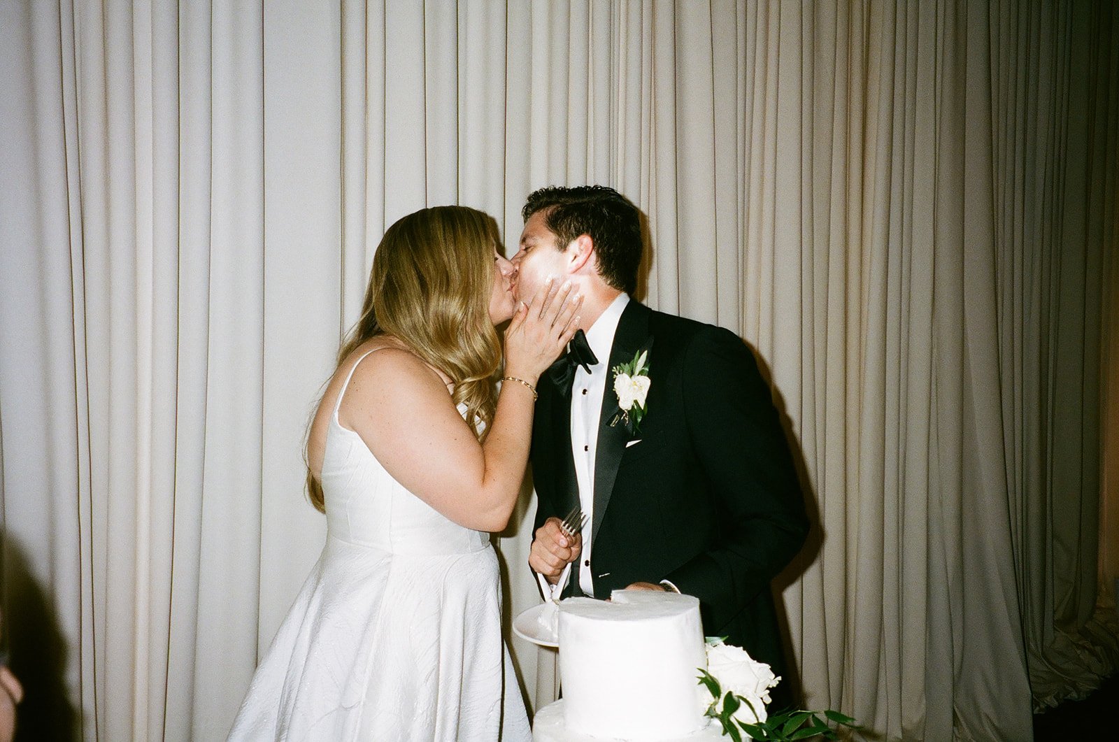 Bride and groom kissing after cutting of the wedding cake on film
