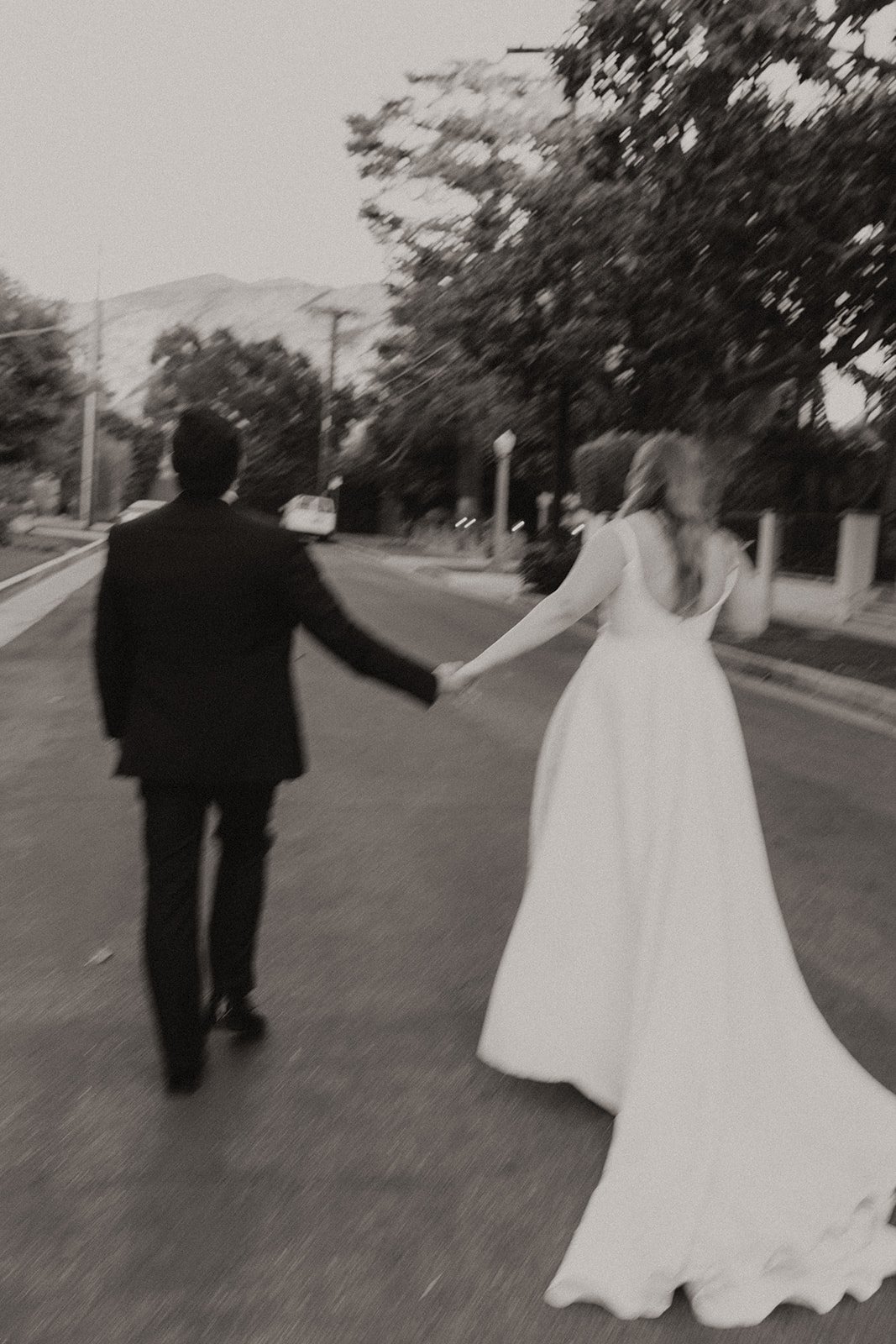 Black and white photo of Bride and groom walking in the street holding hands