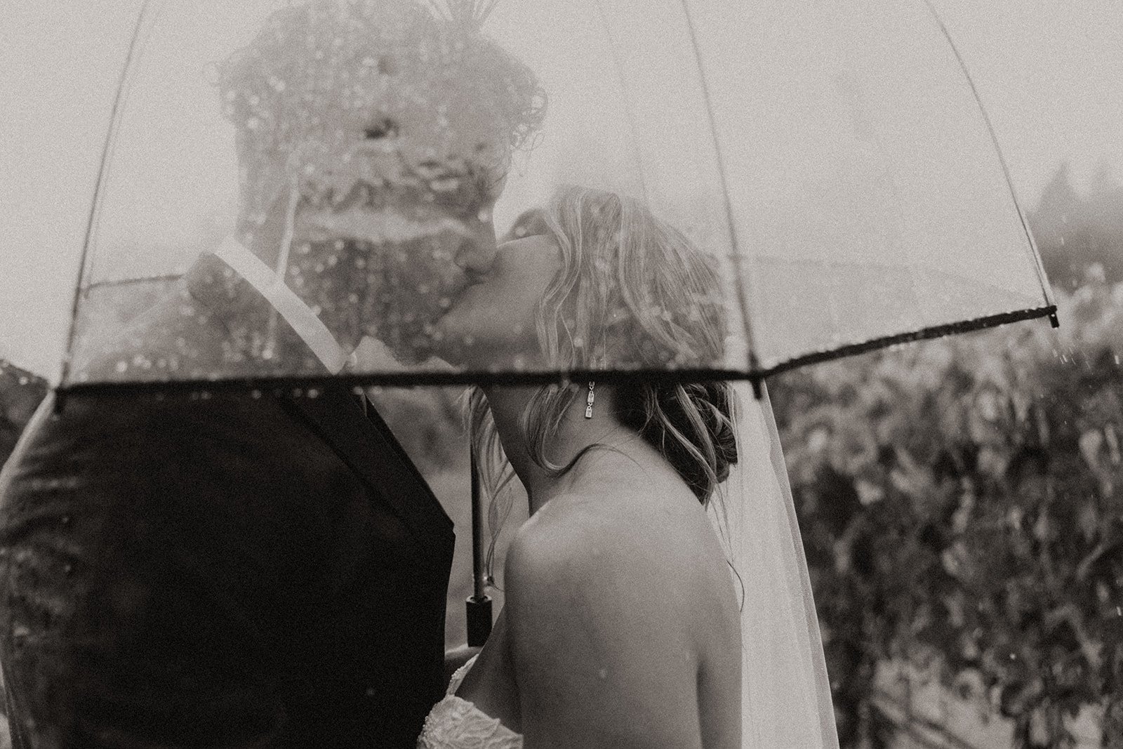 Black and white photo of bride and groom kissing in the rain