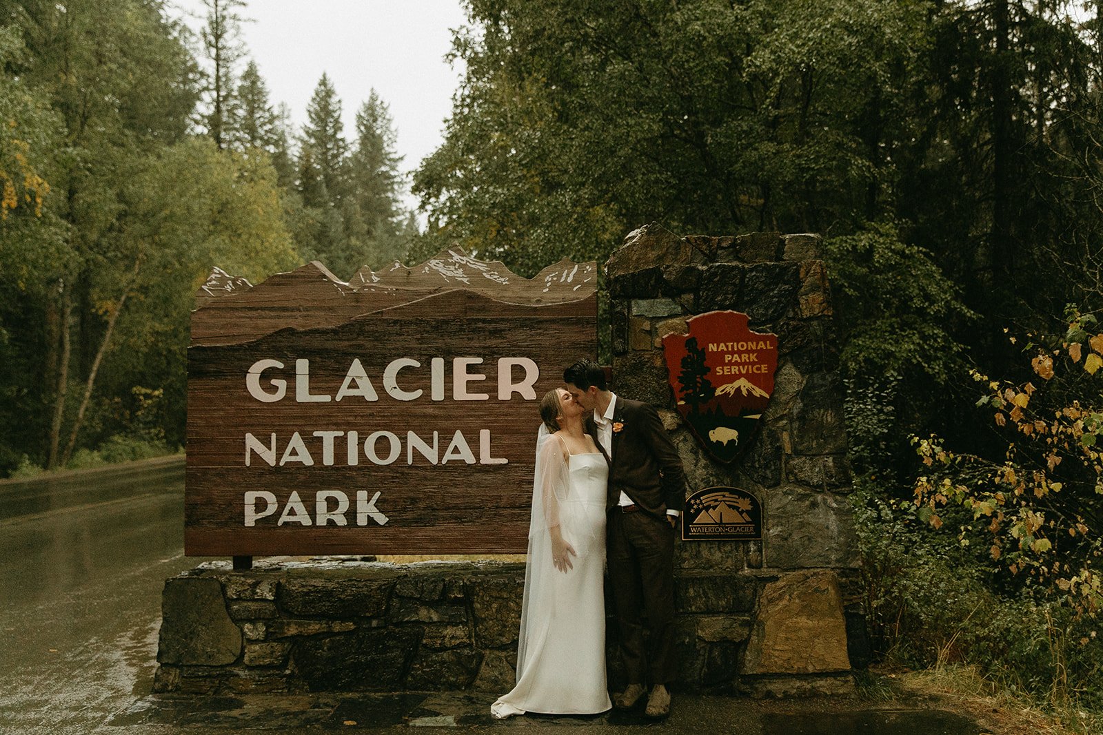 Bride and groom kissing near glacier national park sign
