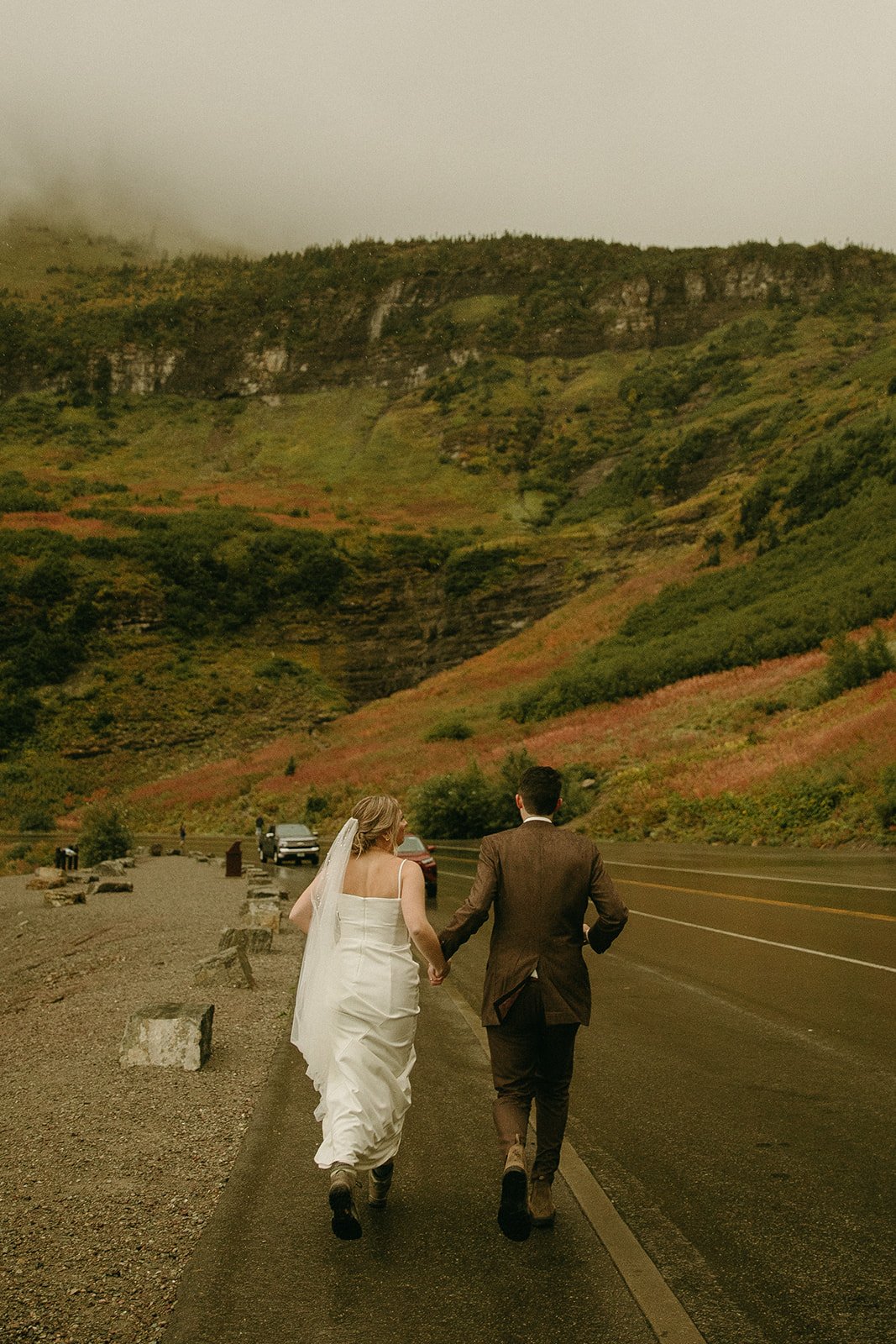 Bride and groom running on the highway in glacier national park