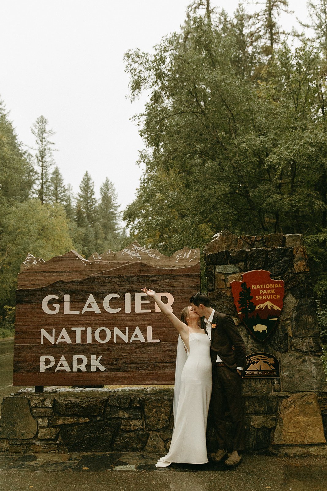 Bride and groom kissing near glacier national park sign