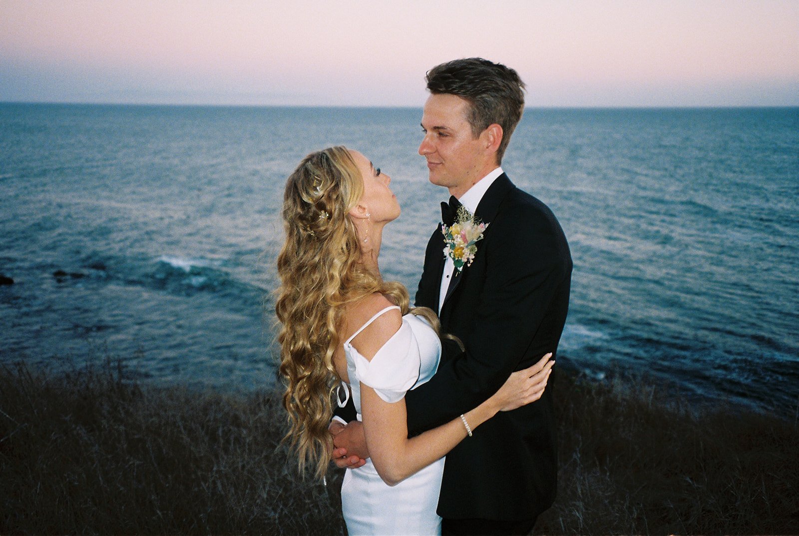 Bride and groom staring into eachothers eyes on the coast on film