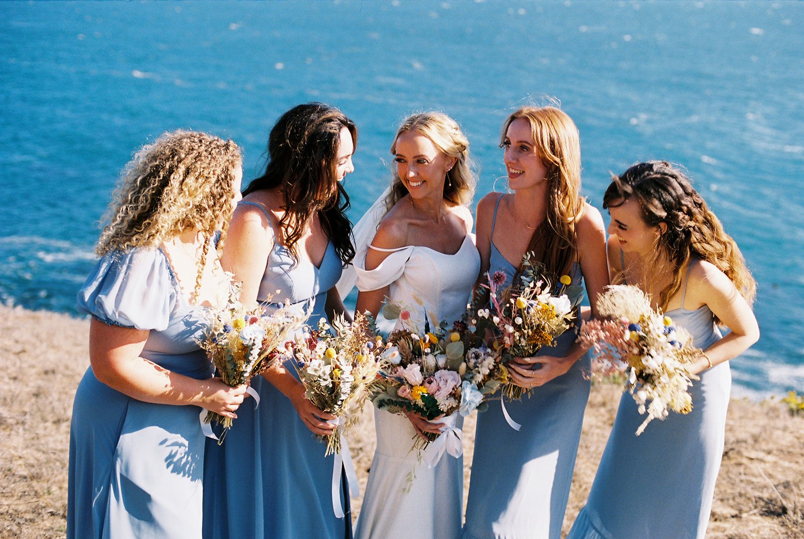 Bride and and bridesmaids smiling on the coast