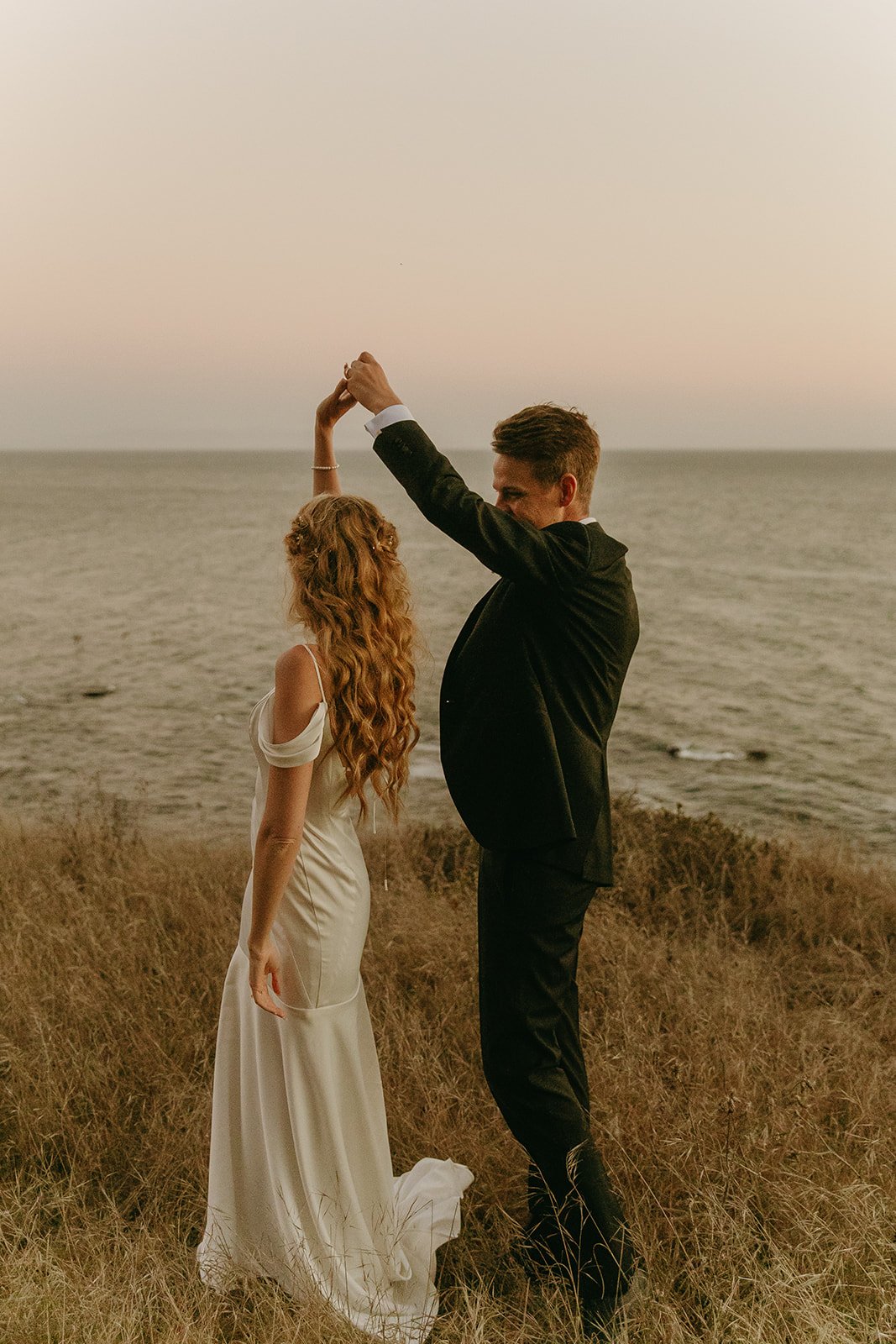 Bride and groom dancing on the coast during sunset