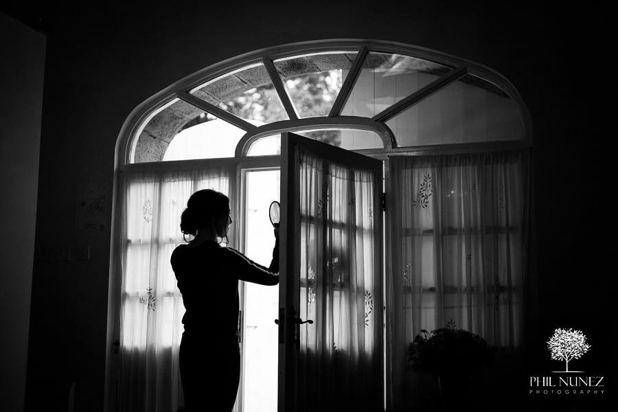 A bridesmaid uses window light to apply her make at Woodhill Hall in Northumberland.