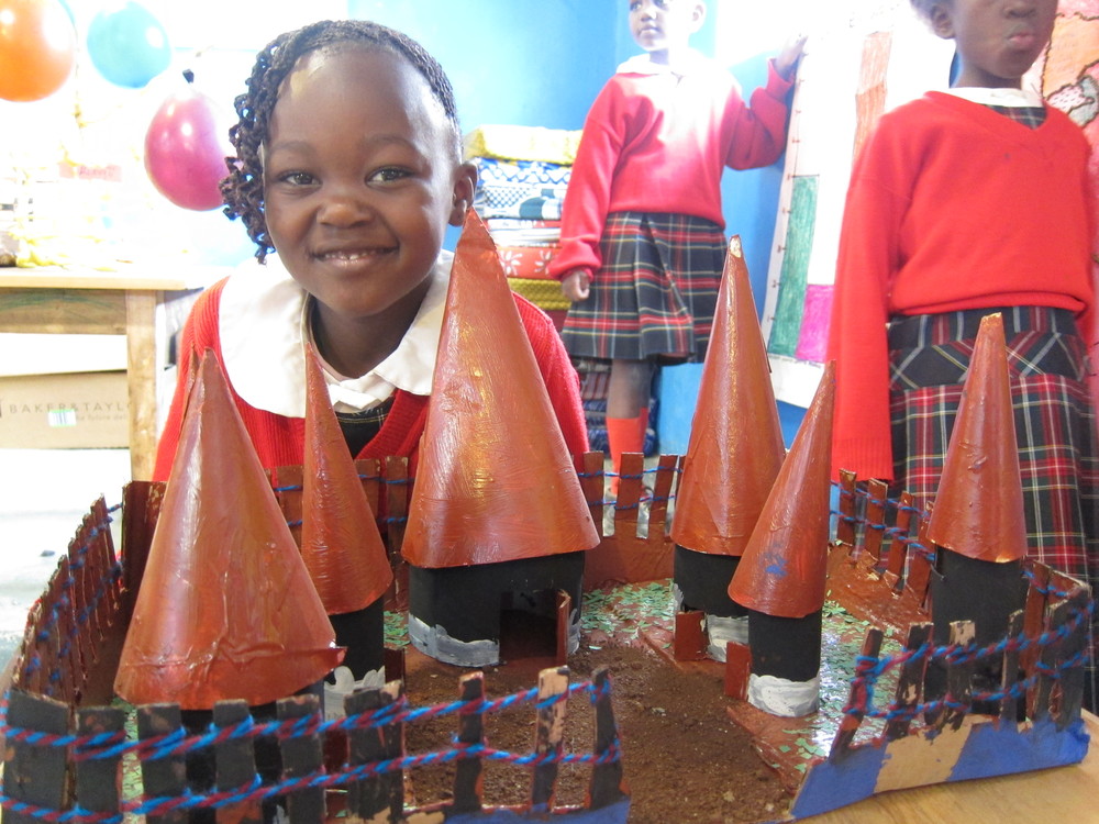 Movin, Kindergarten, hinter einem Modell eines traditionellen Luhya-Dorfes