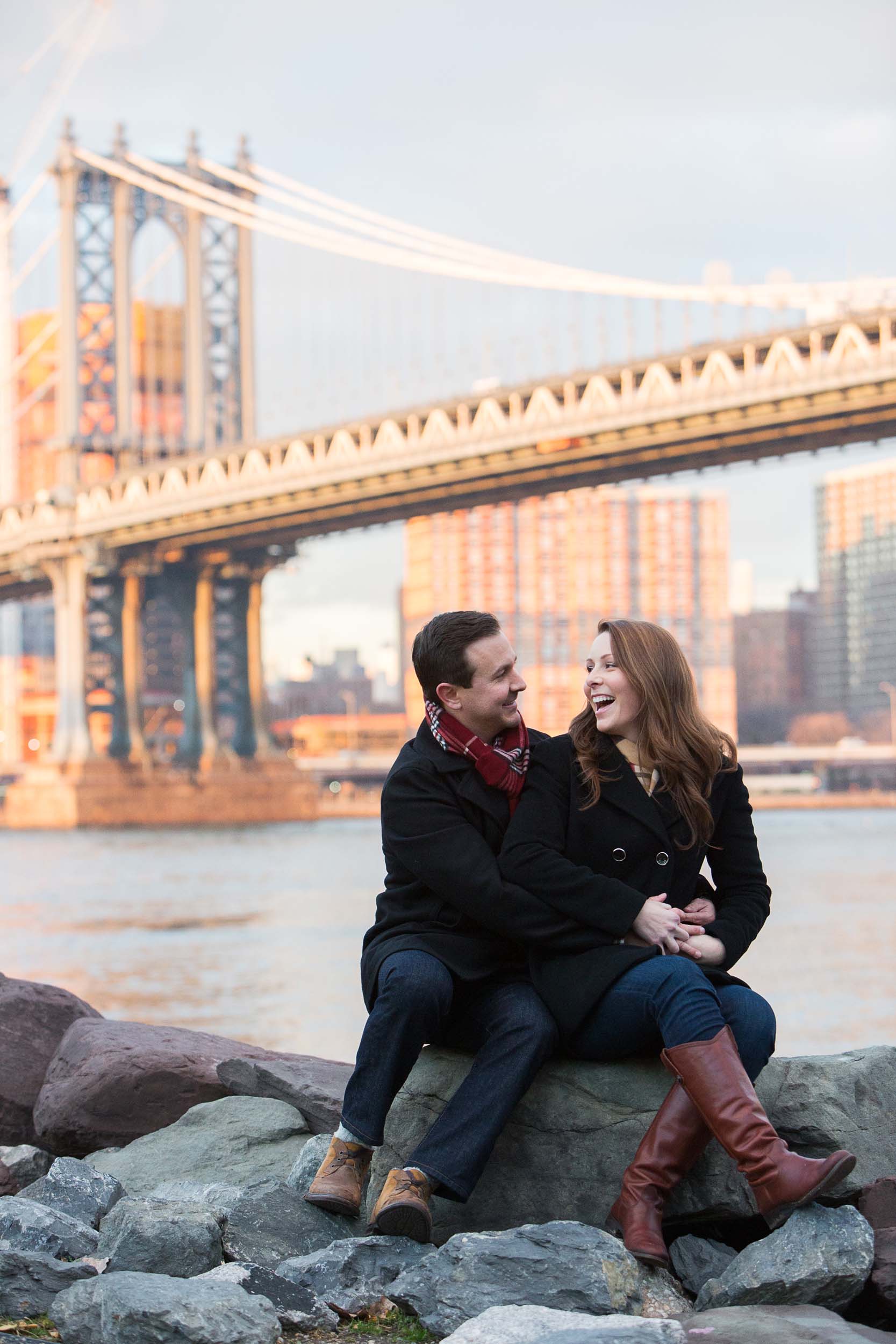 Couple sitting on rocks together laughing with the Brooklyn Bridge in the background in New York City, USA