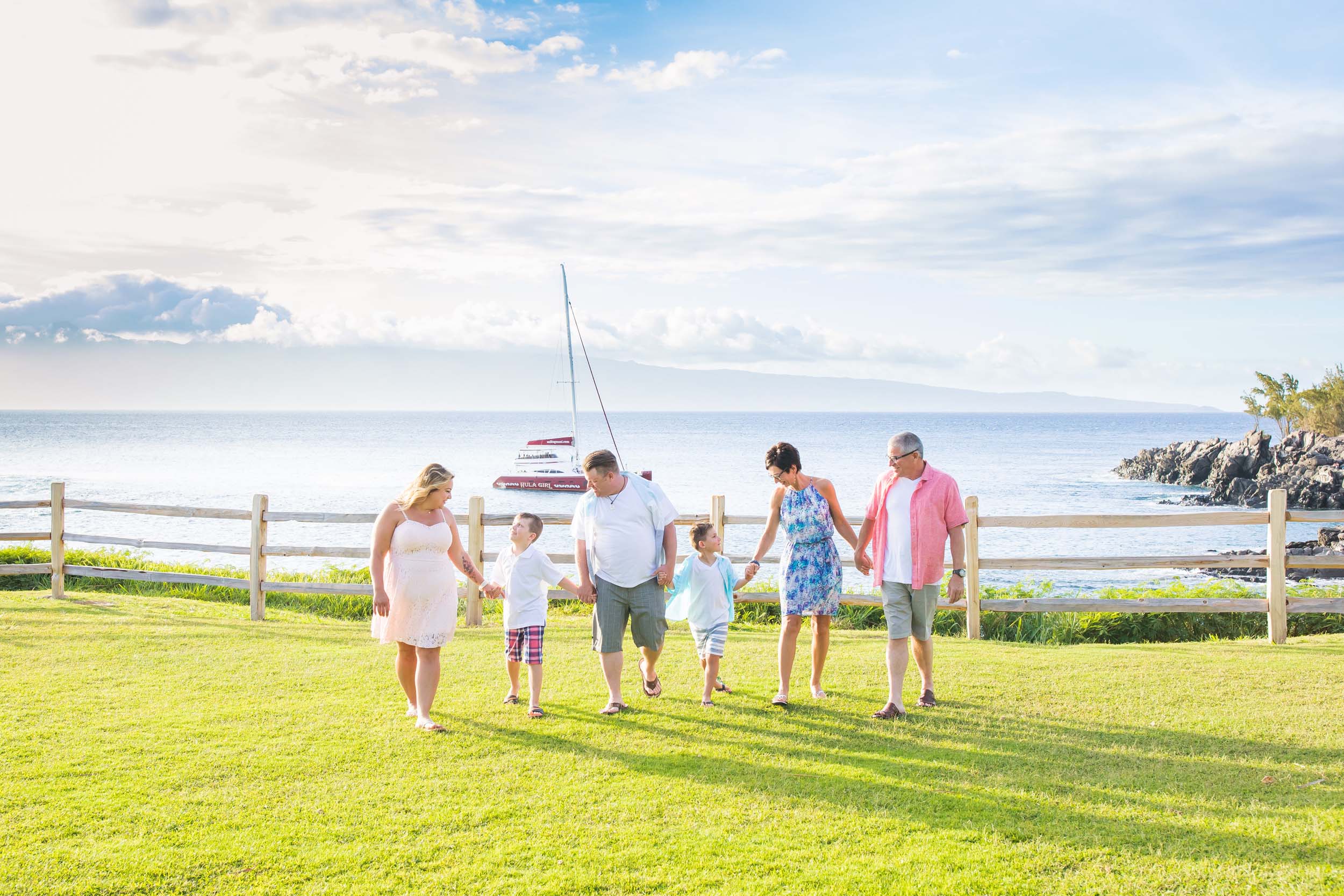 Multi-generational family holding hands and walking along the grass together in Maui, USA