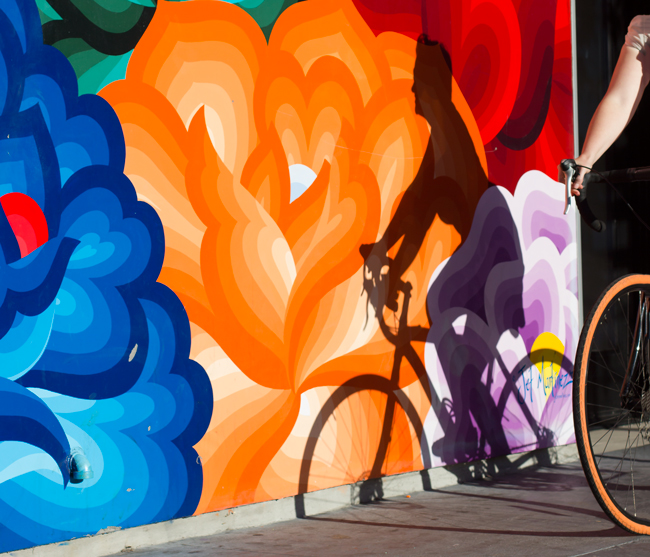 A woman rides a bikes near a mural on San Francisco's Valencia Street