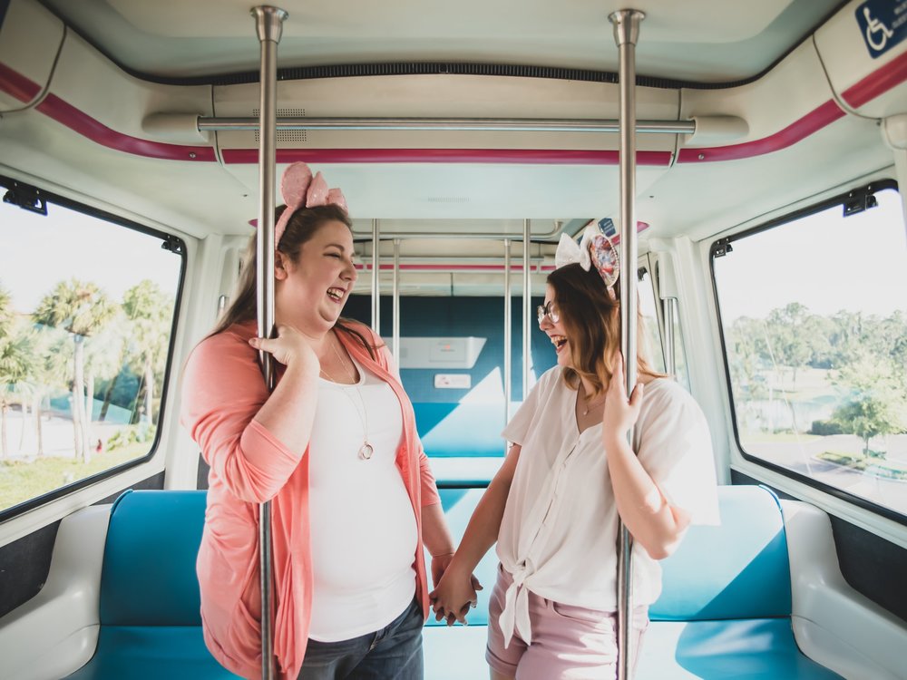 engaged couple holds hands on bus wearing pink mickey mouse ears