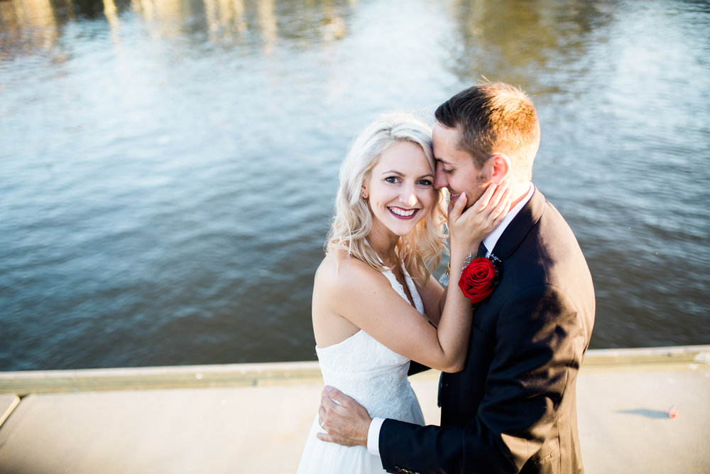 Bride smiling at camera while holding grooms face.
