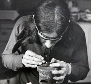 George Yeltatzie in 1975. Copyright Ulli Steltzer. Source: University of Victoria: “Black and white photograph of George Yeltatzie carving a small argillite pendant on a raised mount. Only his upper torso is in view. He is look downward at the carving so that the top of his head is in view. In one hand, he is holding the carving upon a pedestal on a table and carving with a blade in his right hand.”