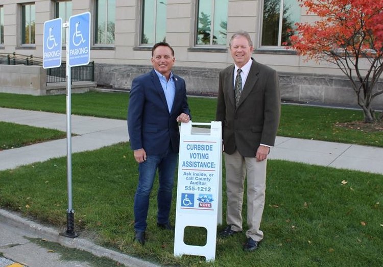 “A lot of voters don’t know curbside voting is an option, so having these signs at each voting location are a big help,” says Secretary Pate (left in photo). Photo from official Facebook page.