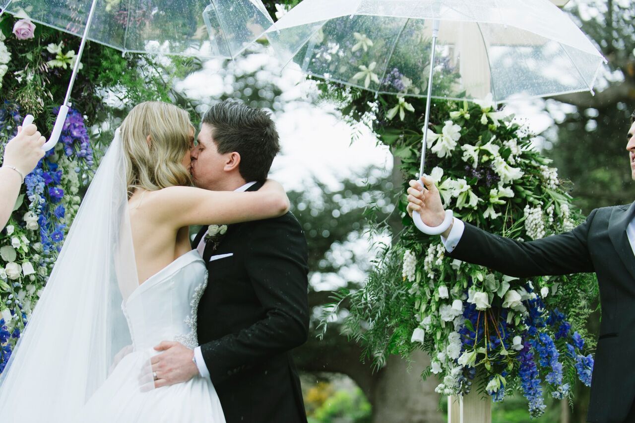 Couple sharing a first kiss at their wedding in the rain under an umbrella