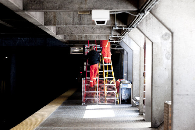 Two people repairing the TTC screens at Eglinton West Station in Toronto
