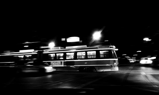 A Toronto Transit Commision TTC street car moving across an intersection at night.