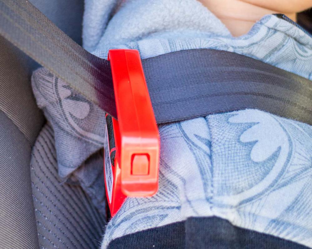 At the back of the foldable booster seat for travel is a long strap that can be hooked onto the shoulder belt of the seat belt. There is a small latch on the shoulder hook that allows the strap length to be adjusted so that the shoulder belt can be pulled down to the proper height for the child.   