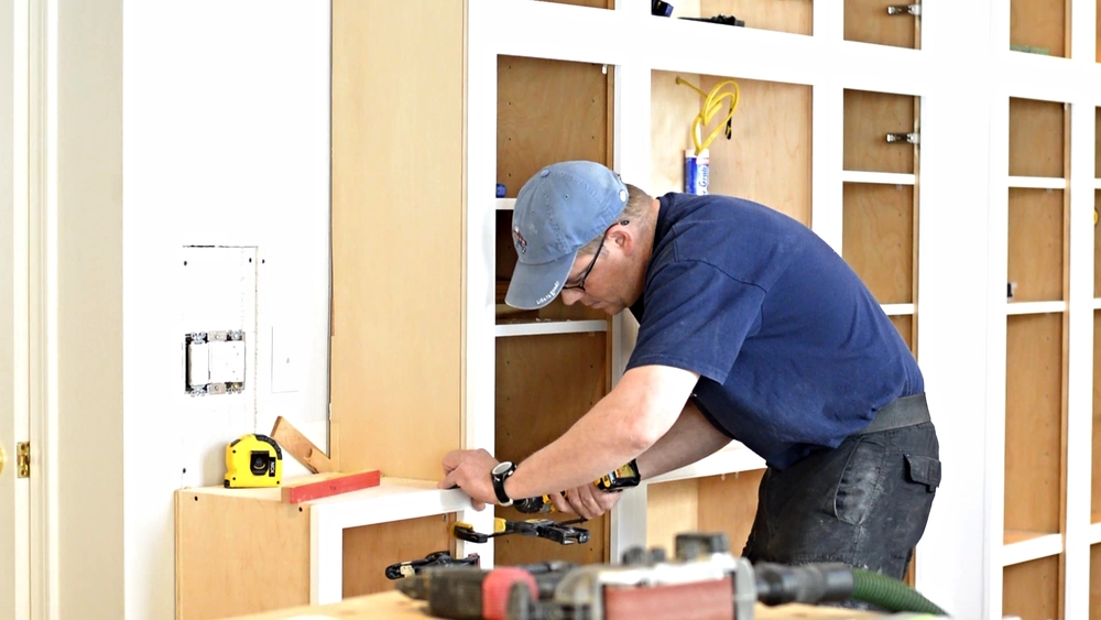 A tradesman working on cabinetry using different tools.