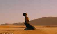 Same woman as in other photos, here from a distance, kneeling in the desert sand, looking up at the sky