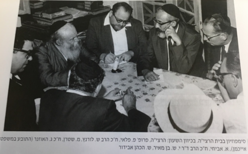 Photo of journalist Pinchas Peli to the left of Rabbi Zevi Yehudah Hakohen Kook, taking notes of the conversation. This symposium took place in the home of Rabbi Kook at 30 Ovadiah Street in the Ge'ulah section of Jerusalem. Peli is seated between Rabbi Kook and MK Rabbi Shlomo Lorincz. Also present during the discussion is Gideon Hausner (who prosecuted Eichmann).
