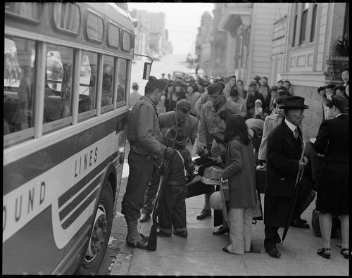  San Francisco, California. The Japanese quarter of San Francisco on the first day of evacuation from this area. About 660 merchants, shop-keepers, tradespeople, professional people left their homes on this morning for the Civil Control Station, from which they were dispatched by bus to the Tanforan Assembly center. This photograph shows a family about to get on a bus. The little boy in the new cowboy hat is having his identification tag checked by an official before boarding. 