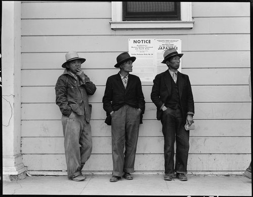 PRINT AVAILABLE April 28, 1942 — Byron, California. Field laborers of Japanese ancestry in front of Wartime Civil Control Administration station where they have come for instructions and assistance in regard to their evacuation due in three days under Civilian Exclusion Order Number 24. This order affects 850 persons in this area. The men are now waiting for the truck which will take them, with the rest of the field crew, back to the large-scale delta ranch.