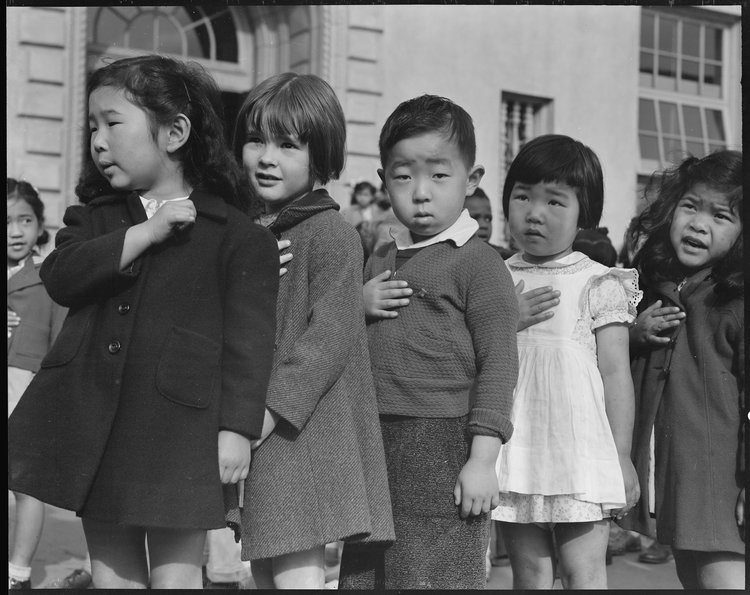 April 20, 1942 — San Francisco, California. Many children of Japanese ancestry attended Raphael Weill public School, Geary and Buchanan Streets, prior to evacuation. This scene shows first- graders during flag pledge ceremony. Evacuees of Japanese ancestry will be housed in War Relocation Authority centers for the duration. Provision will be effected for the continuance of education.