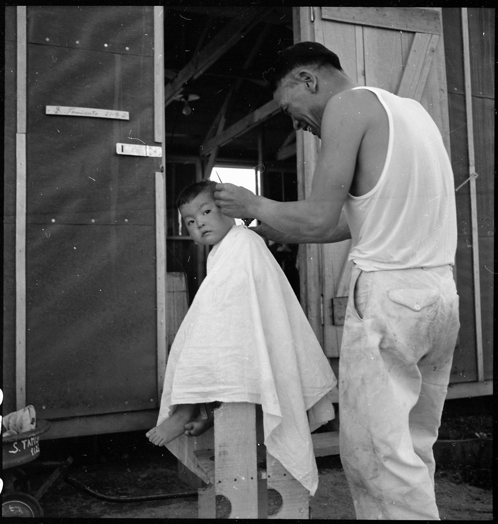PRINT AVAILABLE July 2, 1942 — Manzanar Relocation Center, Manzanar, California. Little evacuee of Japanese ancestry gets a haircut.