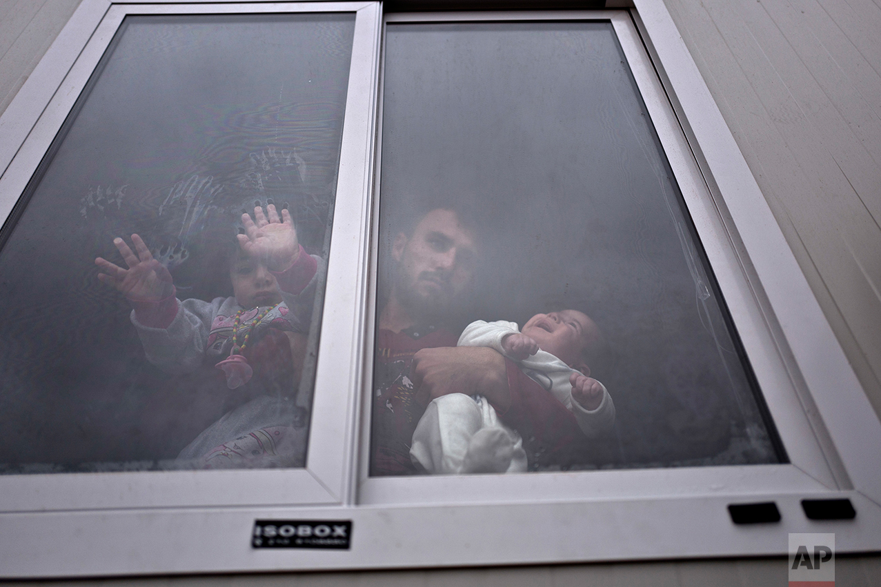 Refugee Siban Assad, 20 years old, from al-Hasaka, Syria, looks out the window of his shelter while holding his daughters, Ruba, one month, and Maldar, 1, at the refugee camp of Ritsona about 86 kilometers (53 miles) north of Athens, Wednesday, Dec. 28, 2016. (AP Photo/Muhammed Muheisen)
