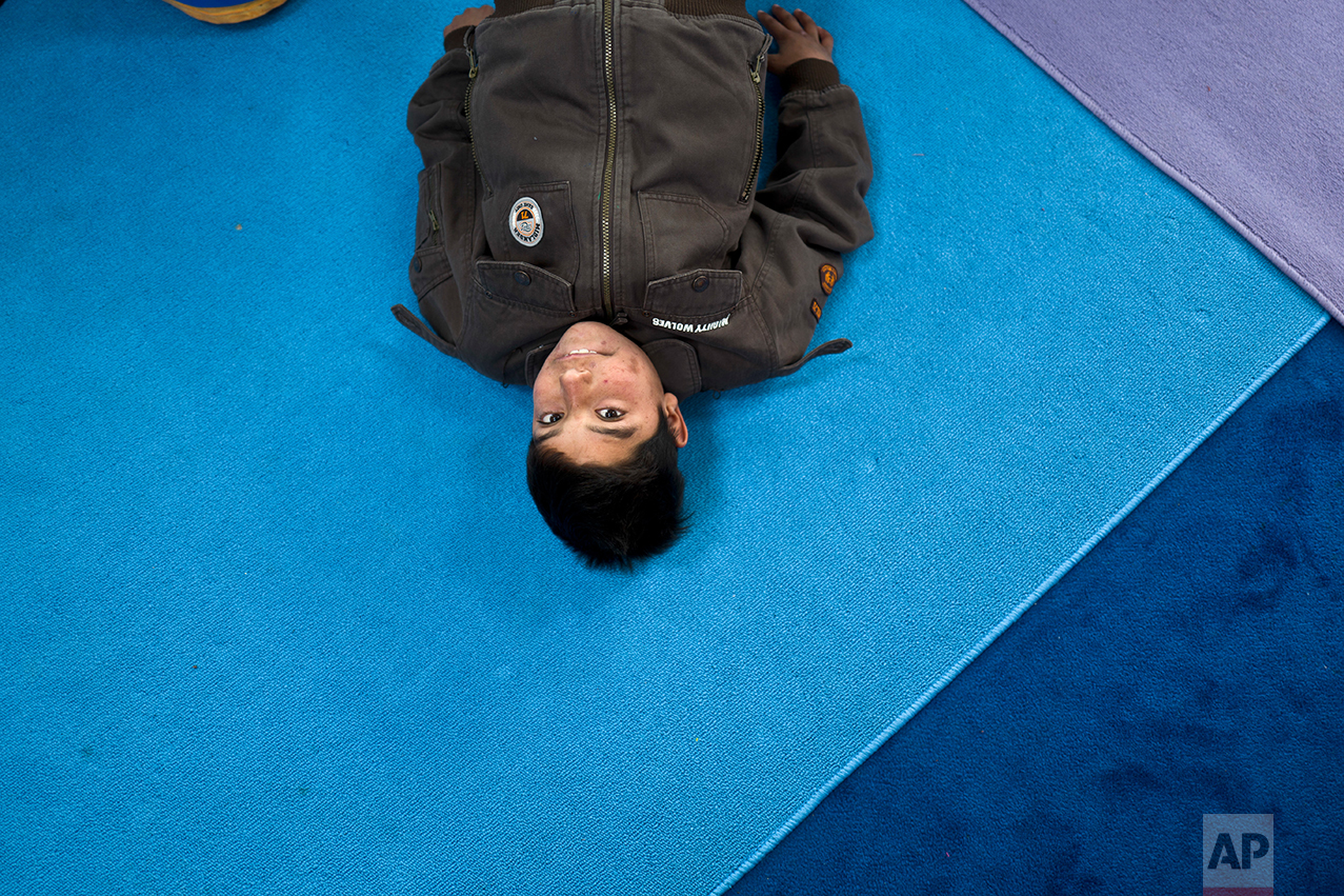 An Afghan refugee boy looks up while attending a yoga session during a class at a makeshift school in the refugee camp of Oinofyta about 58 kilometers (36 miles) north of Athens, Tuesday, Dec. 27, 2016. (AP Photo/Muhammed Muheisen)
