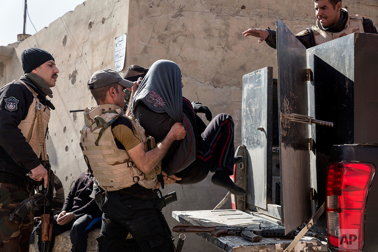 Iraqi security officers place a suspected Islamic State group member into the back of a waiting pickup truck, in east Mosul on Feb. 21, 2017. (AP Photo/John Beck)